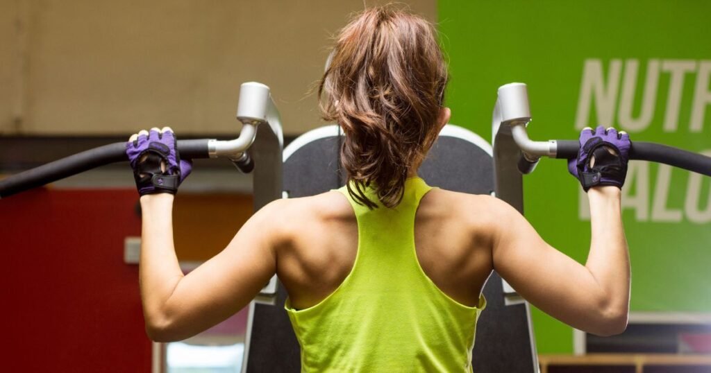 Woman performing a pull-up exercise on an assisted pull-up machine to compare 30 reps per set vs heavy weights for muscle growth and strength training.