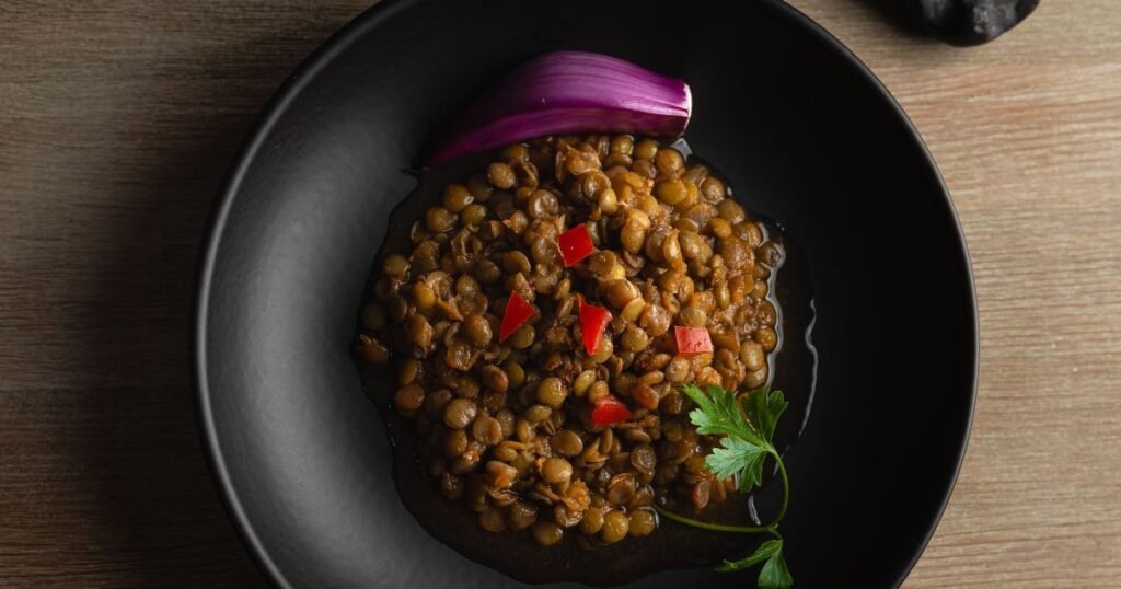 Bowl of cooked lentils garnished with red onion, parsley, and diced peppers, showcasing a healthy high-protein, fiber-rich meal."
