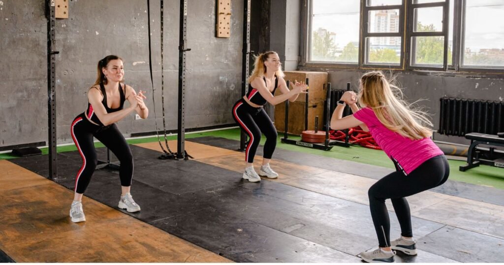 Three women performing bodyweight squats during a 30-minute group workout session in a modern gym to improve strength, fitness, and overall health.